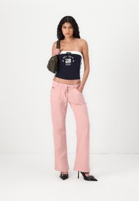 Pink wide-leg trousers with pockets, a navy strapless top featuring white accents and text, and black pointed heels.
