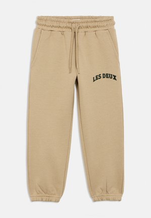 Beige sweatpants met een elastische taille en boorden, zijzakken, trekkoord, en "LES DEUX" in het zwart gedrukt op de linker dij.