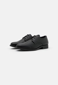 Chaussures en cuir noir avec une finition lisse, bout arrondi et petit talon. Caractéristiques de lacets et de subtils accents de couture sur les côtés.
