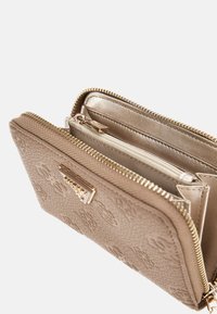 Portefeuille zippé beige avec un extérieur texturé, motif floral, quincaillerie dorée et plusieurs compartiments. L'intérieur doublé présente une finition lisse.