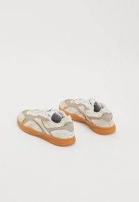 Sneakers albe și bej cu un superior texturat, accente bej și talpă din cauciuc portocalie. Prezintă un logo al brandului pe laterale și un design cu șireturi.