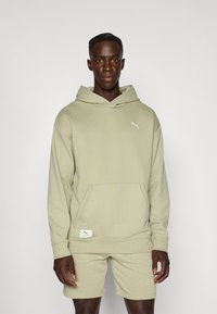 Haut à capuche vert clair en tissu texturé avec une poche devant. Il présente un petit logo Puma blanc sur la poitrine. Assorti à un short de la même couleur.