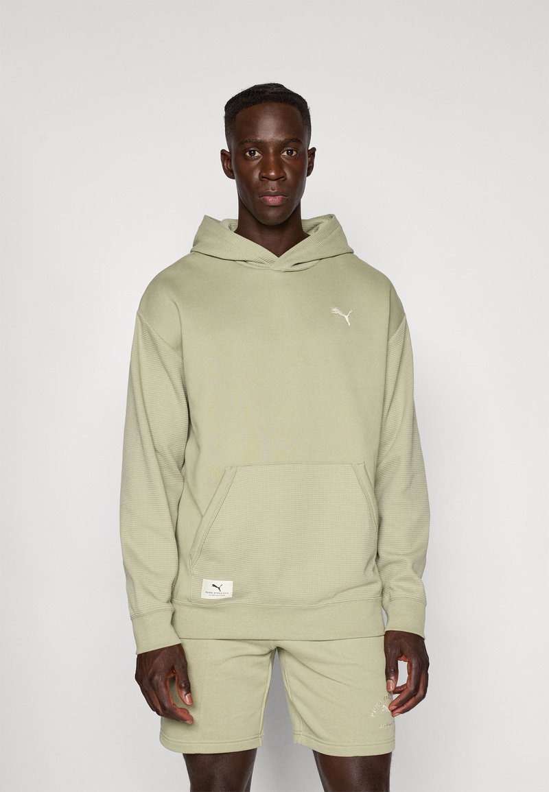 Haut à capuche vert clair en tissu texturé avec une poche devant. Il présente un petit logo Puma blanc sur la poitrine. Assorti à un short de la même couleur.