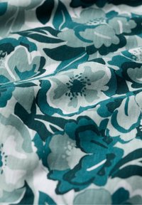 Kwitnąca tkanina w odcieniach turkusu i jasnej zieleni, z dużymi stylizowanymi kwiatami i liśćmi, wydrukowana na białym tle.