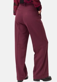 Pantaloni wide-leg borgogna con una texture liscia, dotati di due tasche posteriori e un orlo pulito, abbinati a scarpe con plateau nere.