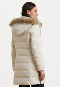 Pufjakas off-white krāsā ar kažokādas oderi kapucei, šūts dizains, garas piedurknes un sānu rāvējslēdzēja detaļa. Gluda tekstūra un silts materiāls.