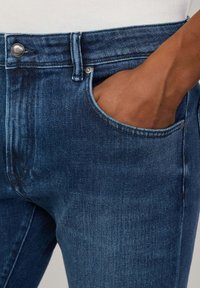 Dunkelblaue Jeans aus Denim mit einem Fünf-Taschen-Design, Metallknopfverschluss und einer glatten Textur mit dezenten Verblassungsdetails.