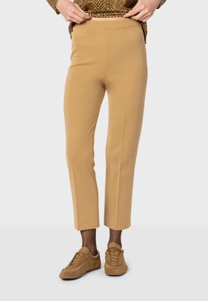 Pantalons en tricot beige au tissu lisse, coupe courte, avec un logo brodé près de la taille, assortis à des baskets en suède.