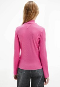 Långärmad rosa ribbad topp med en mock-krage och texturerat mönster, tillsammans med mörka jeans med en figursydd silhuett.