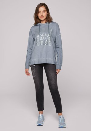 Sudadera azul clara con el texto "SPA DAY" y un patrón texturizado, combinada con leggings gris oscuro que presentan acentos impresos y zapatillas deportivas azules.