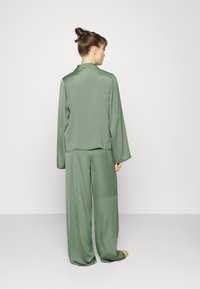Satin grön pyjamas-set som har en långärmad topp med krage och löst sittande byxor, vilket erbjuder en mjuk textur och avslappnad silhuett.