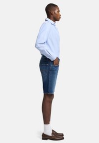 Lyseblå skjorte med knapper, denimshorts, brune loafers og hvide sokker. Shortsene har sidelommer og en baglomme med syning.