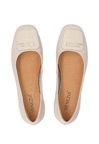 Cream-colored flat shoes with a patent toe cap and embossed logo detail. Smooth exterior, cushioned insole, and rounded shape.