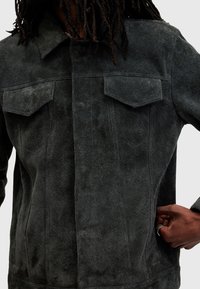 Mörkgrå mockajacka med klassisk krage, två bröstfickor och en texturerad yta. Åtsittande design med knappstängning fram.