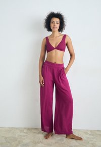 Fuchsia crop top with wide straps and a triangular cut, paired with loose, flowing fuchsia pants featuring an elastic waistband.