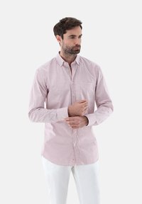 Camicia a righe rossa e bianca in cotone con colletto a punta, maniche lunghe e una tasca sul petto, abbinata a pantaloni bianchi.