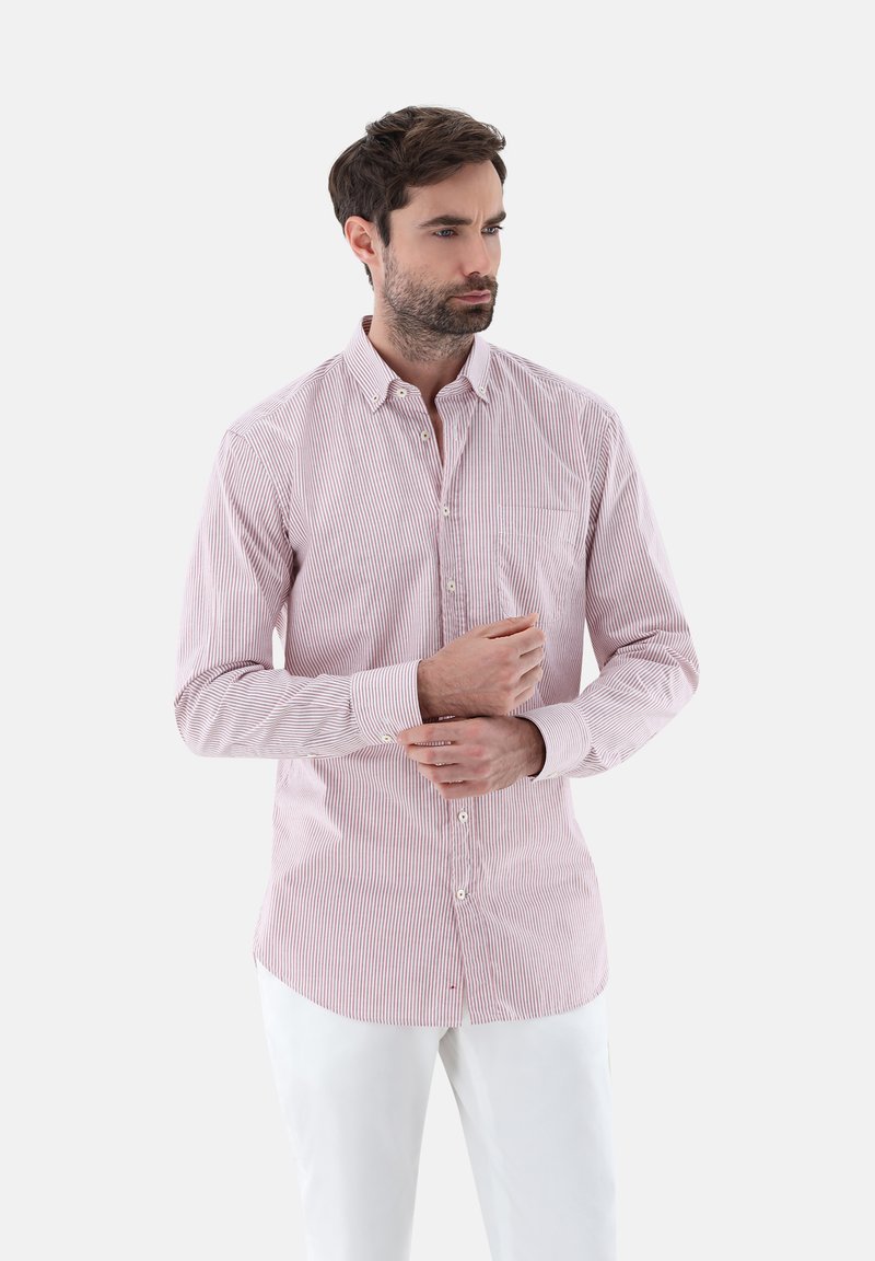 Camicia a righe rossa e bianca in cotone con colletto a punta, maniche lunghe e una tasca sul petto, abbinata a pantaloni bianchi.