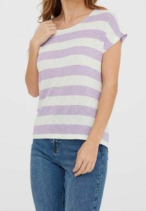 Kobieta w białej koszulce w paski w kolorze lawendowym z krótkim rękawem i niebieskich dżinsach, trzymająca kołnierz koszulki jedną ręką.