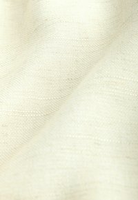 Gros plan sur un tissu doux texturé de couleur blanc cassé avec un motif finement tissé et des plis subtils.