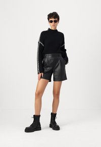 Svart stickad tröja med vita randiga detaljer, kombinerad med högmidjade svarta lädershorts och svarta snörade ankelstövlar.