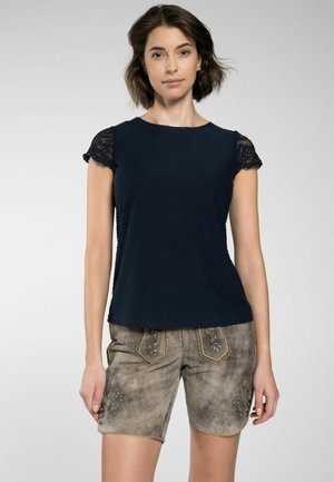 Navy kurzärmliges Oberteil aus strukturiertem Stoff mit Spitzelementen, kombiniert mit beigen Shorts mit floralen Stickereien und kontrastierenden Säumen.