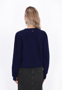 Marineblauer Strickpullover mit puffierten langen Ärmeln und Rundhalsausschnitt. Verfügt über ein kleines Logodetail auf der Rückseite und gerippte Bündchen.