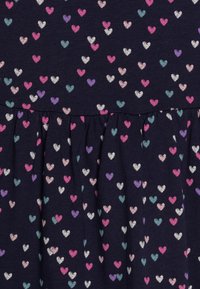 Námořnické šaty z tkaniny s vzorem malých barevných srdcí v růžové, bílé, fialové a tyrkysové barvě, s navrstveným designem sukně.