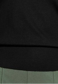 Black knit sweater fabric with a textured finish, featuring a ribbed hem. Paired with light green fabric below, showcasing pleats.
