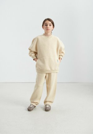 Beige fleece sweatshirt with drop shoulders and front pocket, paired with matching beige sweatpants and animal print shoes.