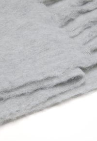 Tessuto di lana grigio chiaro, morbido e peloso al tatto, sovrapposto con pieghe delicate, che presenta un colore uniforme senza motivi o decorazioni.