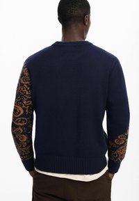 Navy blue knitted sweater with orange patterned accents on sleeves, ribbed collar and hem, fitted design, soft texture, and medium weight.