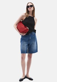 Top senza maniche nero in maglia, pantaloni corti in denim blu con orlo sfilacciato, ballerine nere, borsa rossa con dettagli argentati, occhiali da sole rotondi.