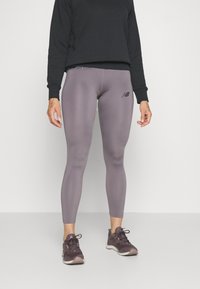 Fioletowe dopasowane legginsy o gładkiej fakturze i haftowanym logo. W połączeniu z czarną bluzą z długim rękawem i ciemnymi butami sportowymi.