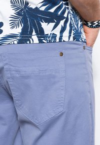 Pantaloni corti azzurri in cotone, con una tasca posteriore con patta, cuciture visibili e un accento in metallo sul bottone.