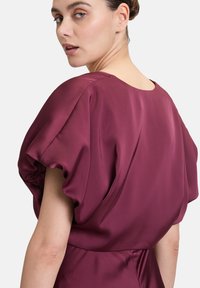 Bordeauxfarbene Satinkleid mit puffierten kurzen Ärmeln, Rundhalsausschnitt und glatter Textur. Es hat eine taillierte Taille und drapierte Details.