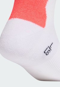 Calzino sportivo bianco con un accento corallo nella parte superiore. Presenta una maglia lavorata a trama e un piccolo dettaglio logo nero vicino al tallone.