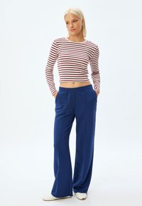 Gestreept langarmtop in wit en bordeauxrode kleur, gecombineerd met losse, blauwe sweatpants met een elastische tailleband, gestructureerde stof en zijzakken.