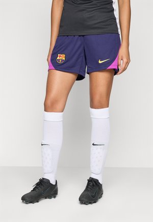FC Barcelona soccer shorts in purple and pink with a logo; paired with white Nike socks and black soccer cleats with turquoise accents.