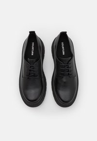 Scarpe in pelle nera con punta arrotondata, design con lacci e suola in gomma. Presenta dettagli cuciti e un interno semplice. Nome del marchio all'interno.