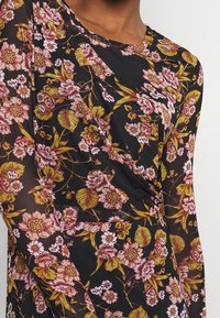 Svart blommig långärmad klänning med rosa och gula blommor, med en mjuk, genomskinlig textur och en rund halsringning.