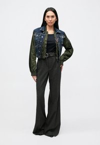 Denim and green bomber jacket with button front, black top, wide gray striped trousers, and black belt with eyelets.