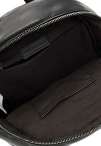 Interno di uno zaino in pelle nera con una texture liscia e opaca; presenta un rivestimento in tessuto nero e una tasca aggiuntiva. Chiusura con cerniera.