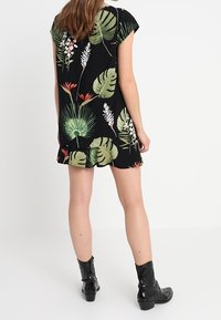 Schwarz kurzes Kleid mit einem tropischen Blumenmuster in Grün und Rot. Verfügt über kurze Ärmel und eine lockere Passform, kombiniert mit schwarzen Knöchelstiefeln.