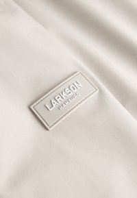 Beige fabric with a stitched rectangular label reading "LARKSON HAMBURG" in raised white letters.