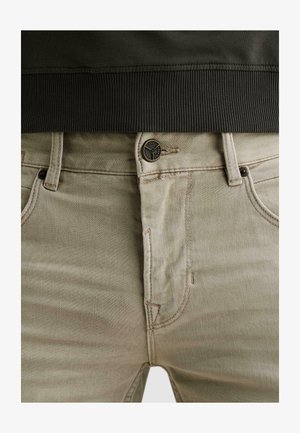 Beige jeans med knaplukning mærket "PME Legend" og synlige bæltestropper, parret med et mørkt ribbet linningstøj.