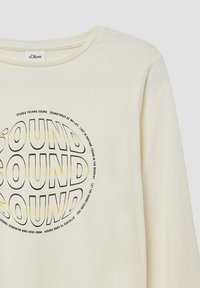 Crème-kleurig langemouwen shirt met een cirkelvormige grafiek waarin de tekst "SOUND" in zwart en geel is weergegeven, met aanvullende zinnen rondom de rand.