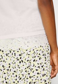 T-shirt com bainha de renda com ondas em branco, sobreposta a uma saia amarela estampada com manchas de leopardo em preto e lavanda. Textura de tecido macio.