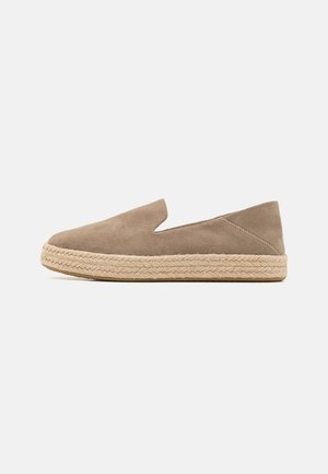 Lässiger Slip-On-Schuh mit hellbraunem Wildleder-Obermaterial und dicker geflochtener Jutsohle vor weißem Hintergrund.