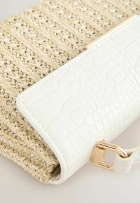 Pochette en paille tissée avec un rabat en cuir synthétique blanc texturé, rehaussée d'une fermeture à boucle en métal doré. Présente une couleur naturelle avec une finition lisse.