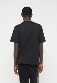 Fekete pamut póló kerek nyakkivágással, rövid ujjakkal és laza szabással. A hátoldal egyszínű, logók vagy minták nélkül.